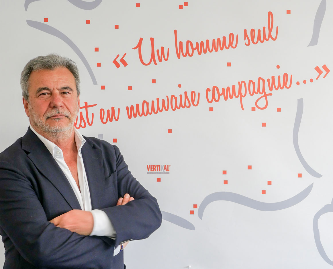 Portrait d’homme en costume bras croisés devant une citation murale